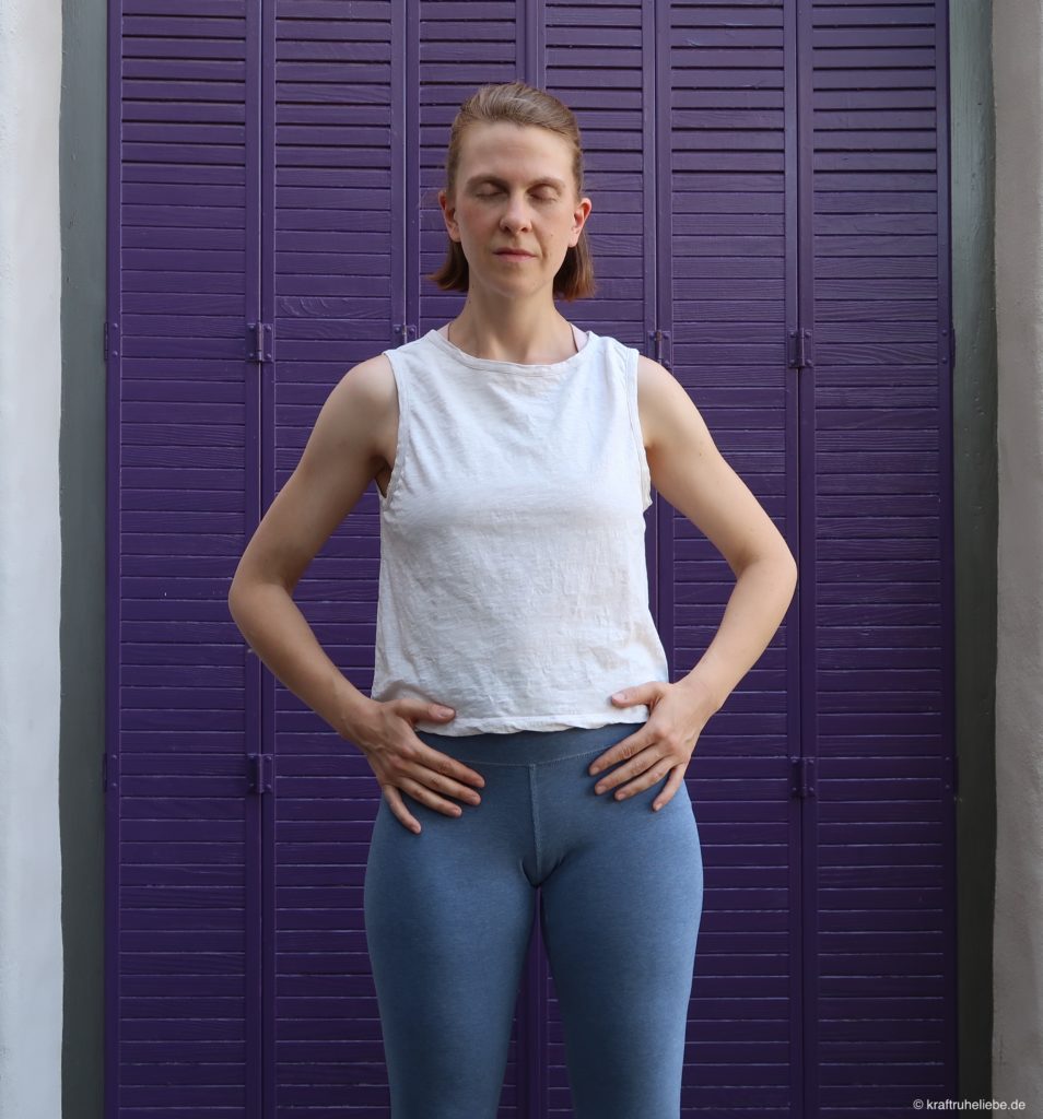Eine Frau im Yogaoutfit steht mit geschlossenen Augen vor einer lila Wand
