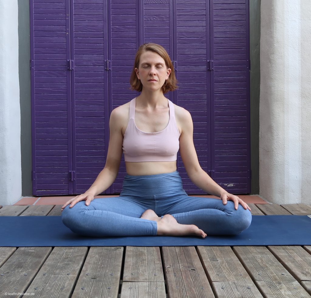 Eine Frau in Yogakleidung sitzt im Schneidersitz auf einer Yogamatte