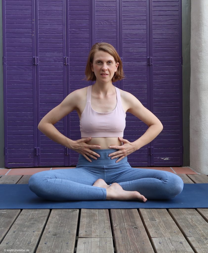 Eine Frau in Yogakleidung sitzt auf einer Yogamatte