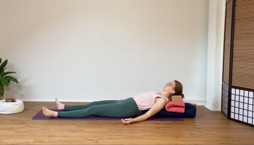 Psoas Entspannung: eine Frau liegt auf einer Yogamatte, hochgebockt auf einem Bolster