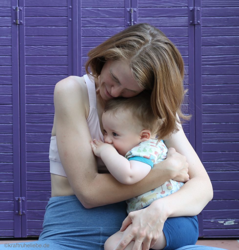 Eine Frau hält ein ca. einjähriges Baby im Arm, während sie auf einer Yogamatte sitzt