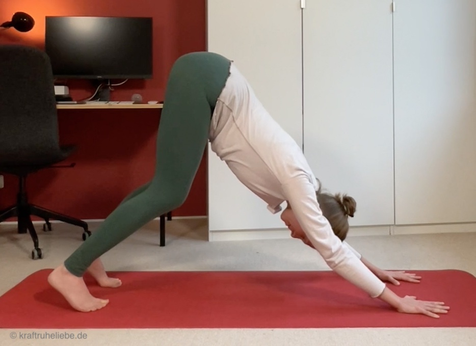 Eine Frau in Yogakleidung übt die Hundestellung Kopf nach unten auf einer roten Yogamatte