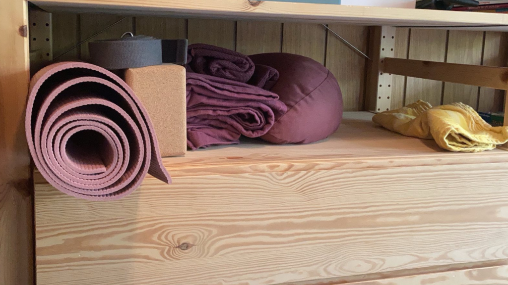 Blick in ein Holzregal, in dem Yoga Equipment liegt