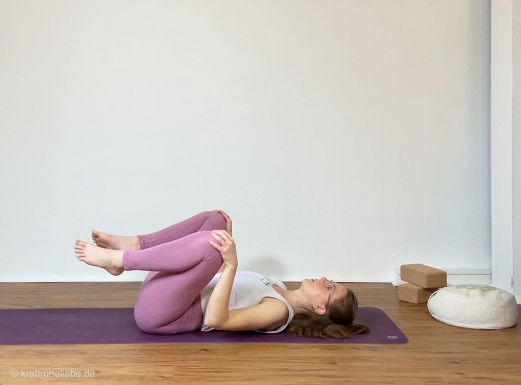 Beckenmobilisierungen zur sanften Beckenbodenaktivierung: eine Frau in pinken Yogaleggings demonstriert Hüftkreisen im Liegen