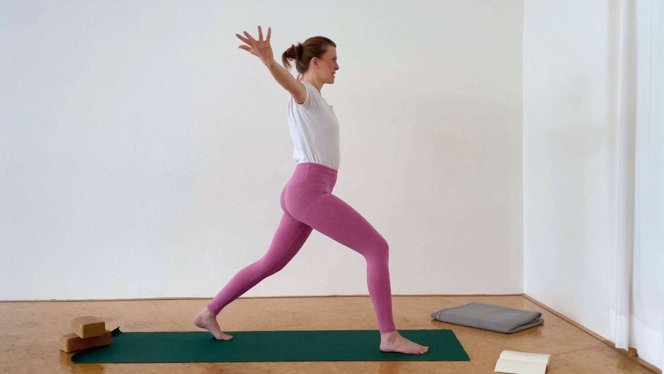 Eine Frau in pinken Yogaleggings demonstriert eine Krieger-Variante mit Schulteröffnung