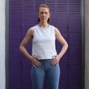 Eine Frau im Yogaoutfit steht mit geschlossenen Augen vor einer lila Wand