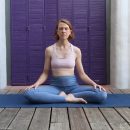 Eine Frau in Yogakleidung sitzt im Schneidersitz auf einer Yogamatte