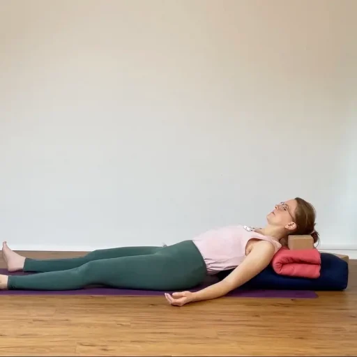 Psoas Entspannung: eine Frau liegt auf einer Yogamatte, hochgebockt auf einem Bolster