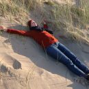 Eine Frau in rotem Pulli liegt entspannt ausgestreckt in den Dünen