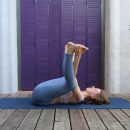 Frau mit blauer Yogaleggings übt eine Yogaübung in Rückenlage